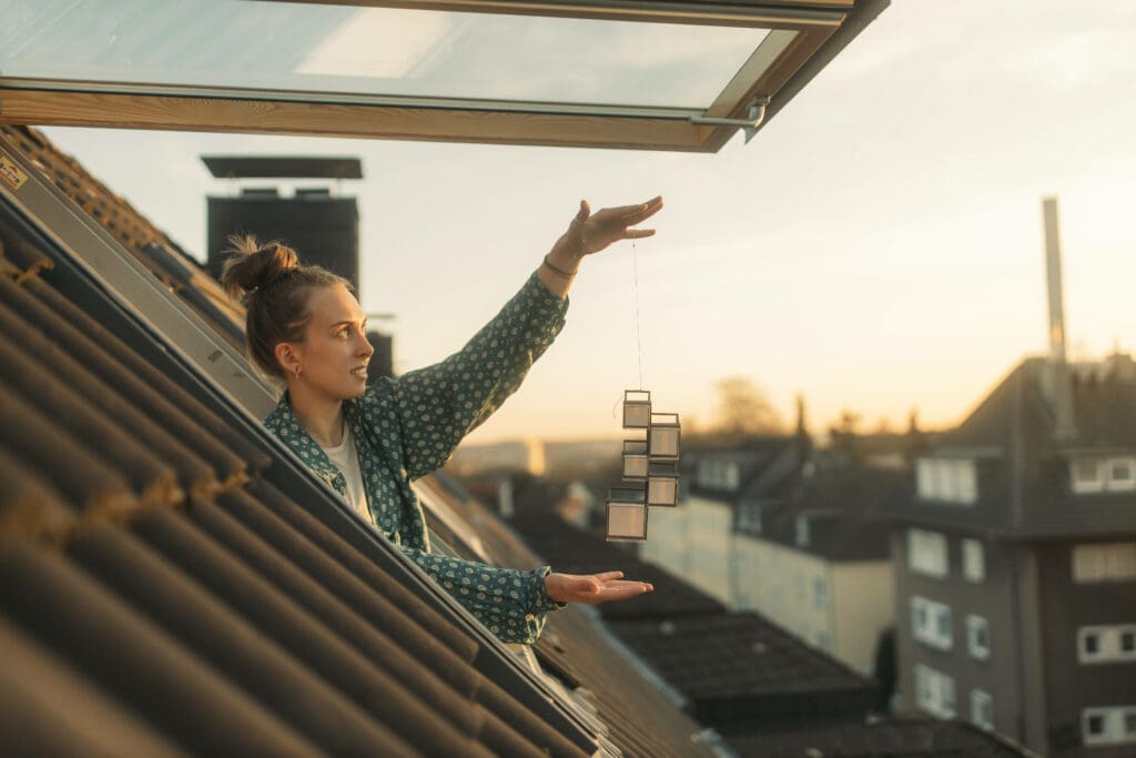 Junge Frau hält Windlichter aus dem geöffneten Dachfenster