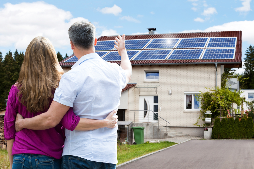 Paar steht vor Einfamilienhaus mit Solarzellen auf dem Dach