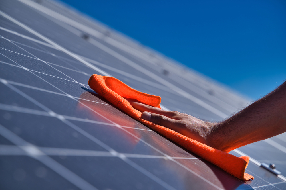 Hand mit orangem Lappen beim Reinigen einer Solaranlage