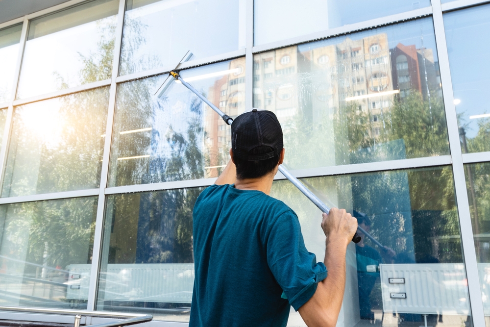 Ein Mann der mit einer langen Stange das Fenster putzt